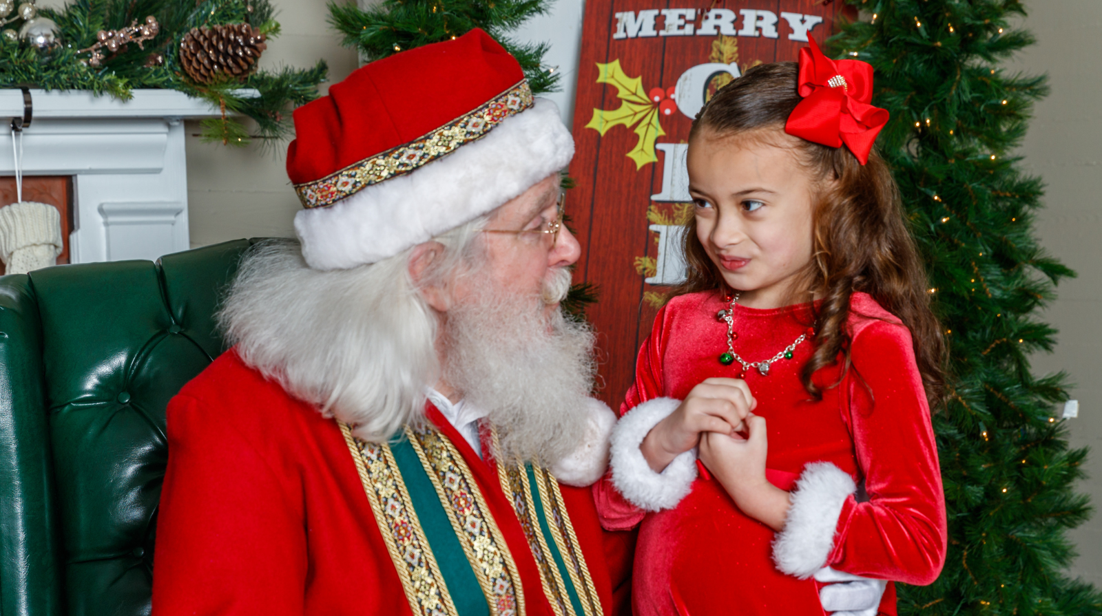 A little girl sits beside Santa Claus during the A Day with Santa event in downtown Kennesaw, capturing a joyful holiday moment.