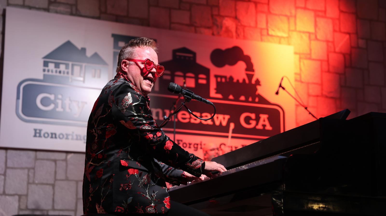 A man in a bright red suit engages in playing a piano, blending style with his musical performance.