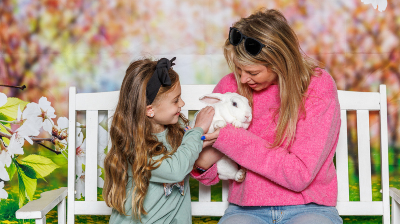 A woman and a young girl sit on a bench, joyfully holding a rabbit during the Kennesaw Bunny Breakfast event.
