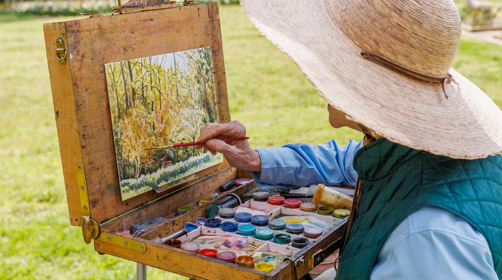 An person paints on an easel in a field, participating in an art workshop at Smith-Gilbert Gardens.