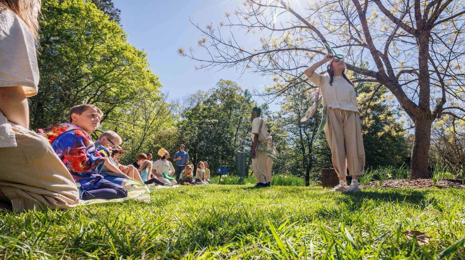 A group of college age students performing a play in a garden in front of kids
