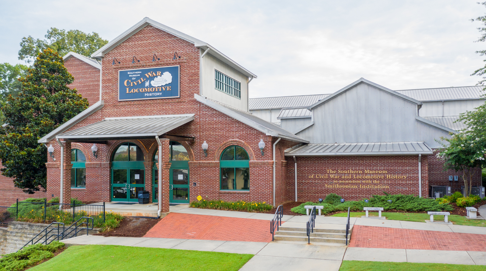 Red-brick building with a sign for a Civil War and Locomotive History museum. Arched windows, green doors, and a manicured lawn create a welcoming atmosphere.