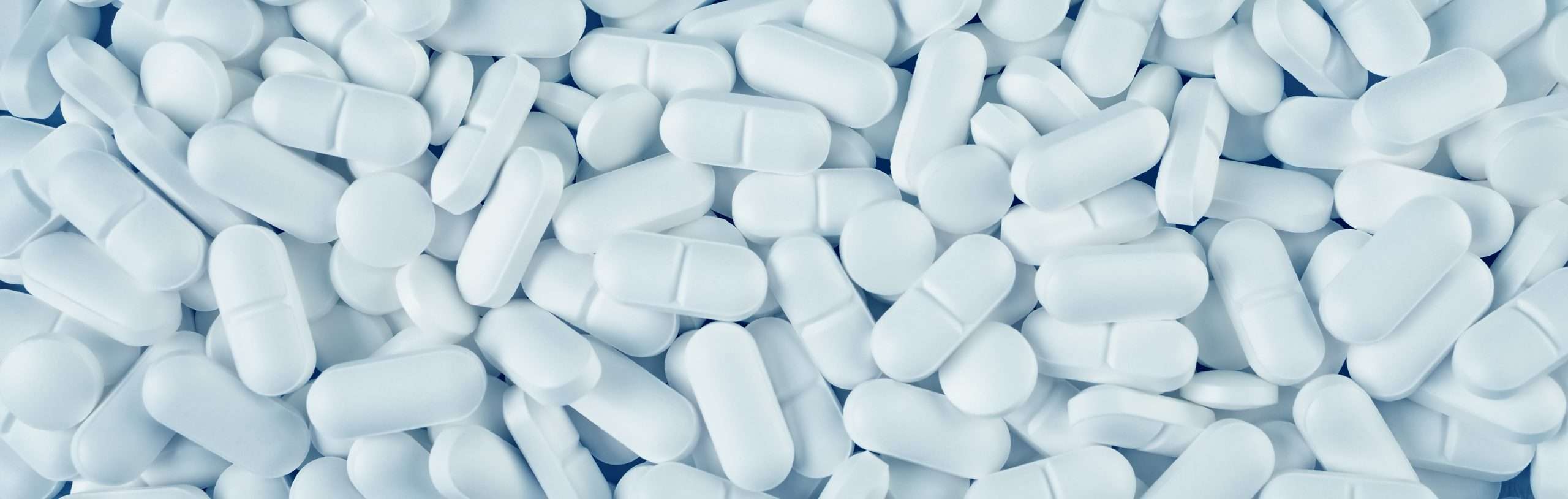 Pills spilled on blue background. A lot of white tablets