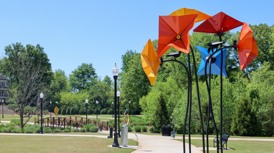 A colorful sculpture in a park with a wooden bridge in the background